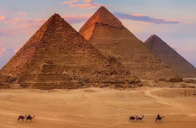 The great pyramids of Giza in Egypt UNESCO World Heritage Site at sunset in hues of orange color with tourists riding camels next to the pyramids