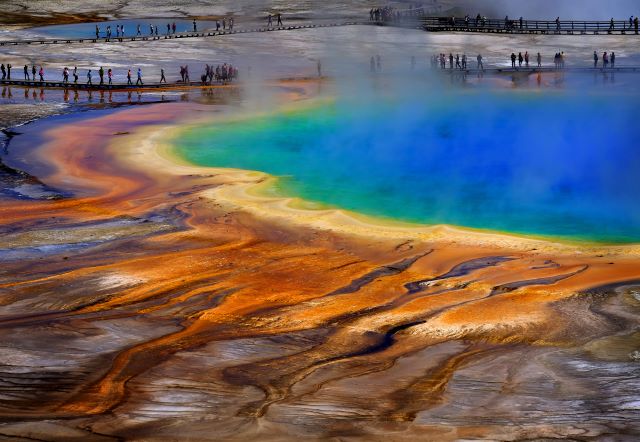 Yellowstone National Park UNESCO World Heritage Site geothermal pools with bright colors of the hot steam and water and tourists hiking round the hot springs pools